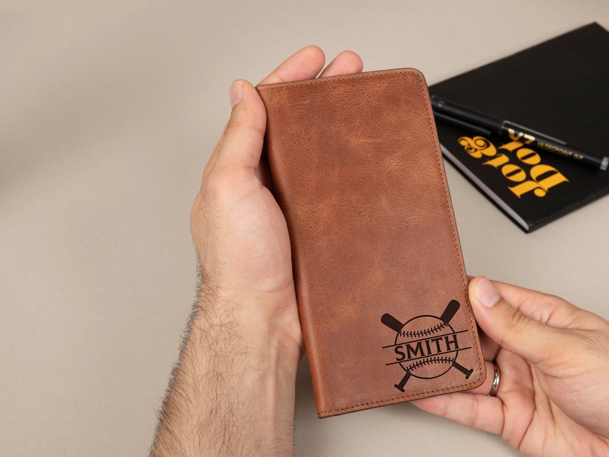 Baseball Long Wallet • Personalized Genuine Leather Wallet - The Lush Gifts - Baseball Long Wallet • Personalized Genuine Leather Wallet - The Lush Gifts - The Lush Gifts - Card Holder - Black - a man holding a brown leather wallet next to a book - Customized Leather Gift - Personalized Leather Gift